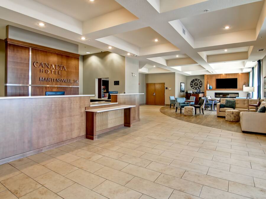 A spacious lobby with a reception desk, a seating area with sofas and a dining table, and a large flat-screen TV mounted on the wall.