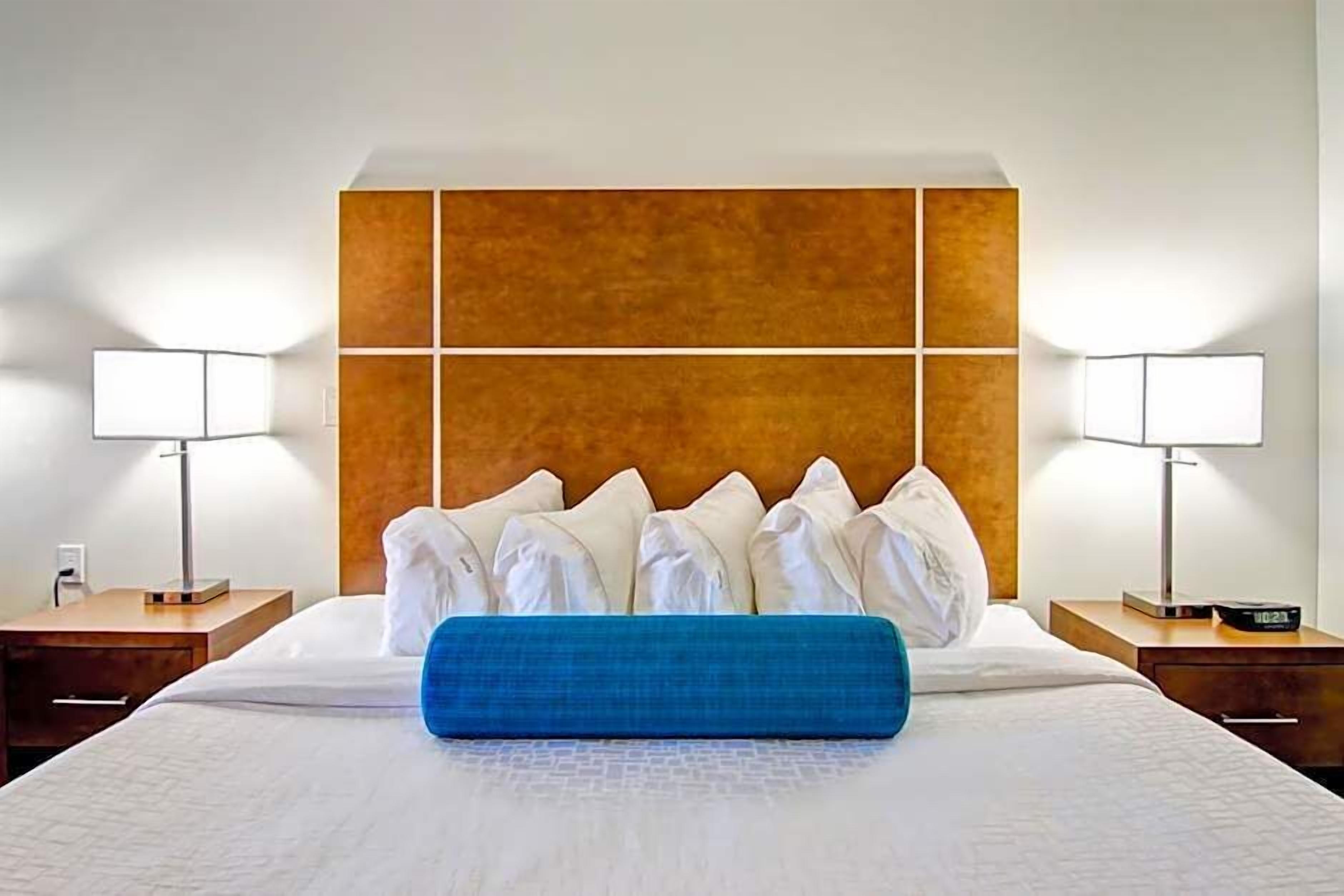 A hotel room with a large bed, two bedside tables, a wooden headboard, and two wall-mounted lamps.