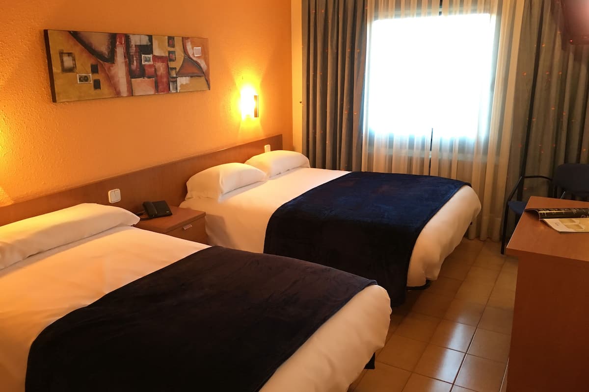 Habitación de hotel con dos camas, un escritorio, una lámpara y un cuadro en la pared.