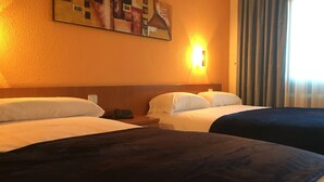 Habitación de hotel con dos camas, un cuadro en la pared, una mesita de noche con teléfono y una ventana con cortinas.