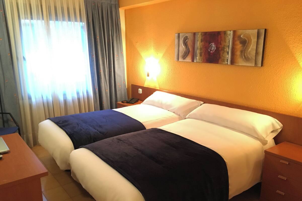 Una habitación de hotel con dos camas, un escritorio, una mesita de noche y un cuadro en la pared.