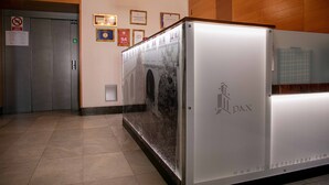 A reception area with a white reception desk, a wall-mounted sign, and a framed certificate. - Hospedería Pax (León)