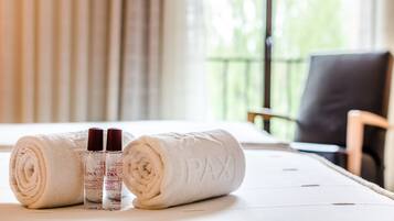Ein ordentlich bezogenes Bett mit aufgerollten weißen Handtüchern und zwei Flaschen PAX Körperlotion.