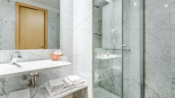 Un baño moderno con lavamanos de mármol, ducha con cerramiento de vidrio y toallas ordenadamente dobladas.