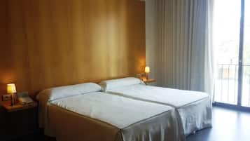 Una habitació d'hotel amb dos llits, un panell de capçalera de fusta, una taula de nit amb una làmpada i una finestra gran amb cortines.