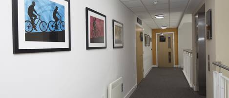 A hallway with framed artwork on the walls, a radiator, and a door at the end.