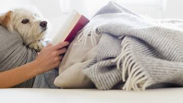 Una persona acostada en la cama con un perro, leyendo un libro.