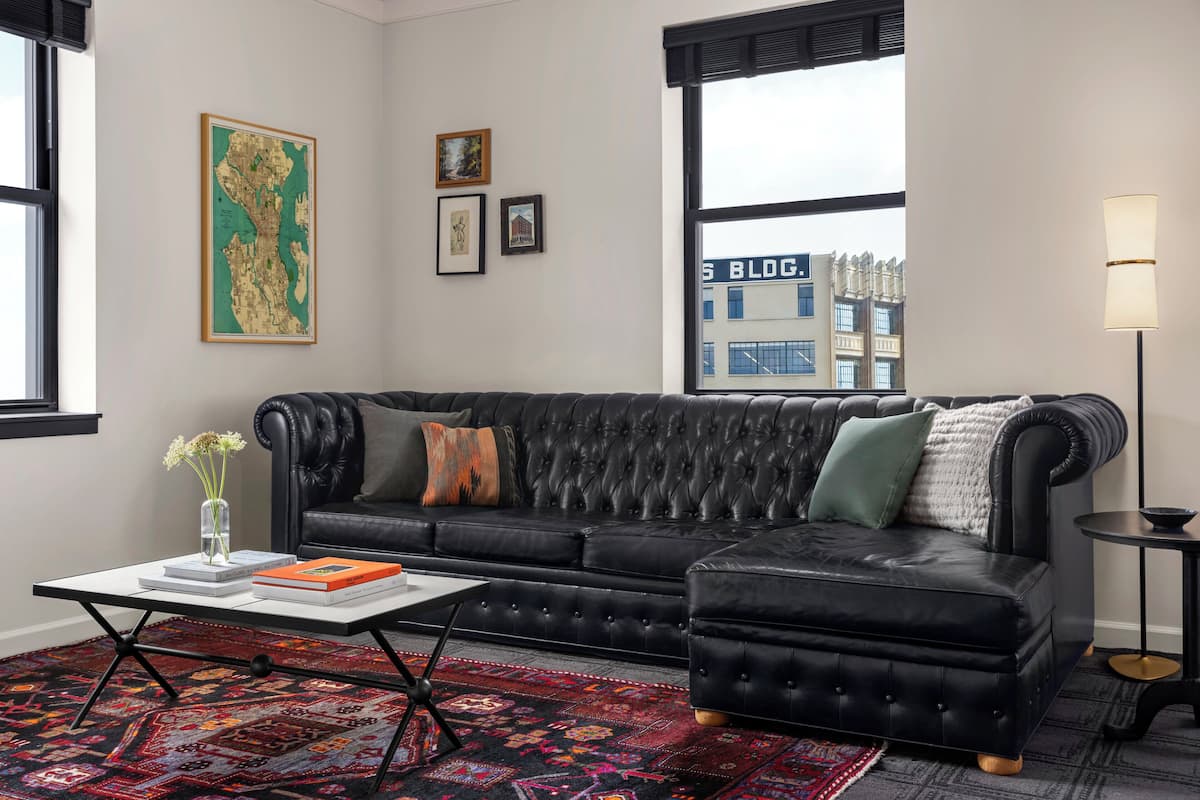 A modern living room with a black leather sofa, a coffee table, and a patterned rug.