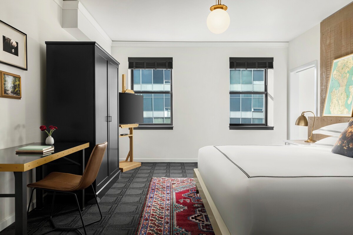 A modern bedroom with a bed, a desk, a chair, a wardrobe, and two windows.
