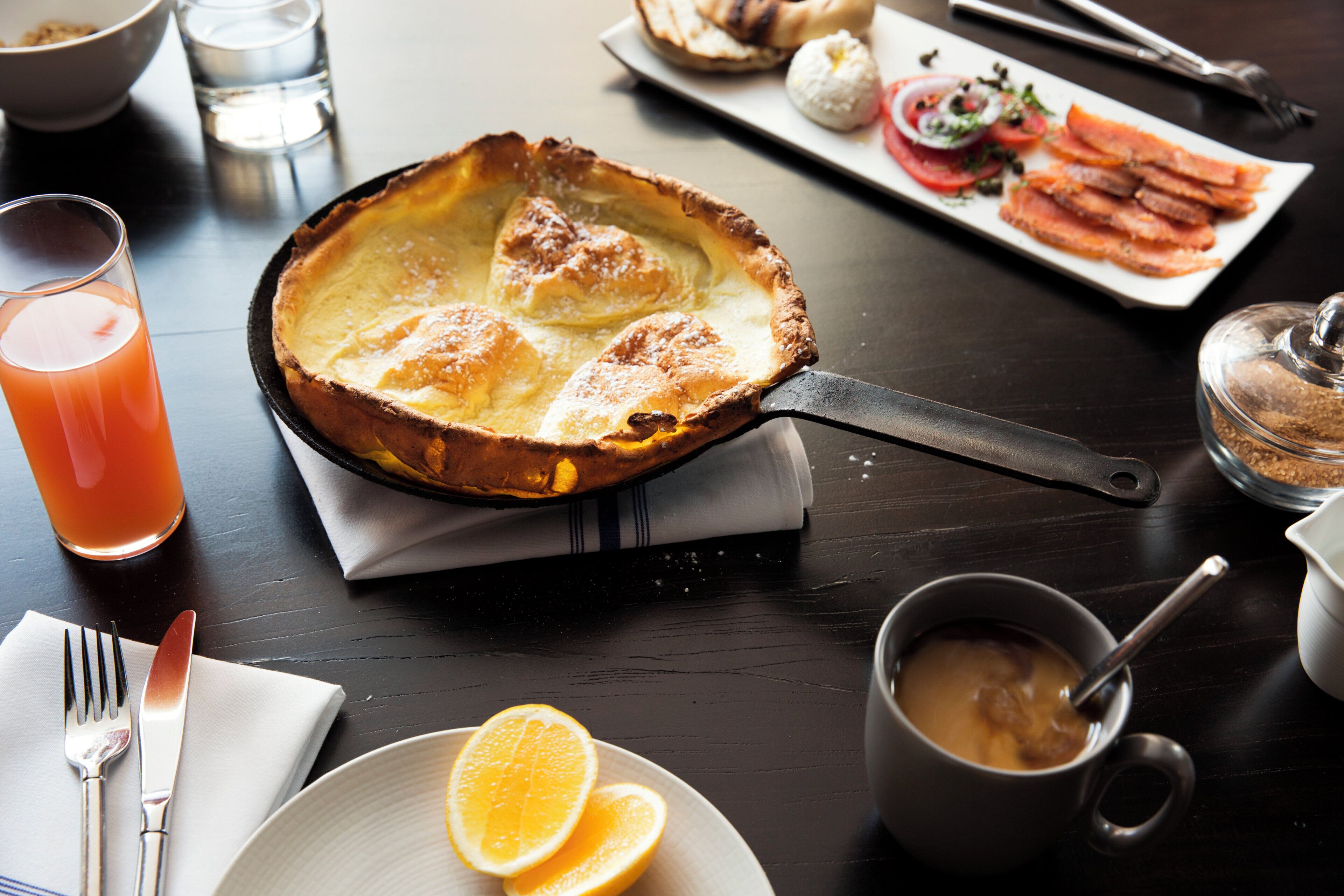 Un desayuno con un pastel de ricota, rodajas de naranja y una taza de café sobre una mesa.