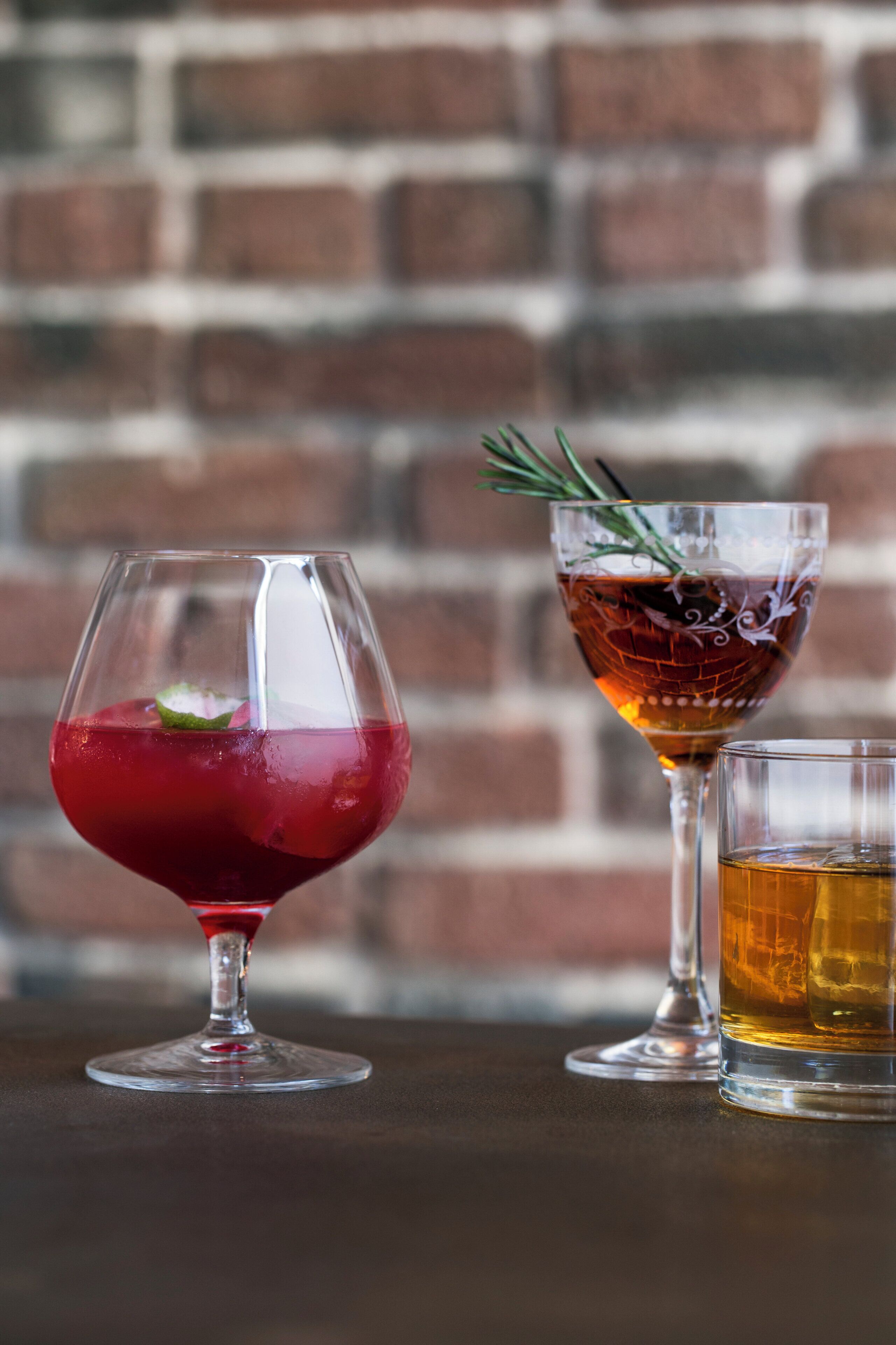 Tres vasos de bebidas distintas sobre una mesa, con un fondo de pared de ladrillo.