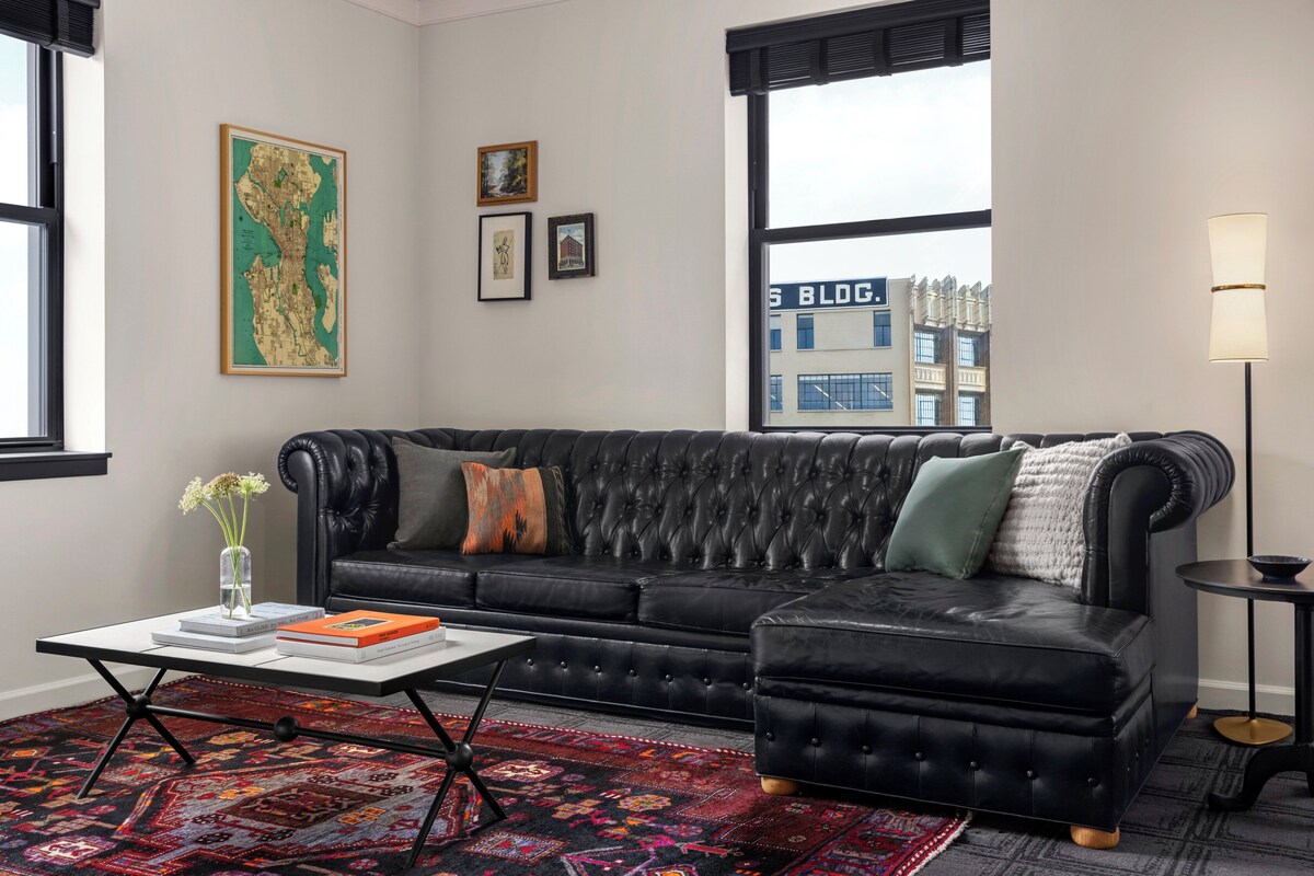 A modern living room with a black leather sofa, a coffee table, and a patterned rug.