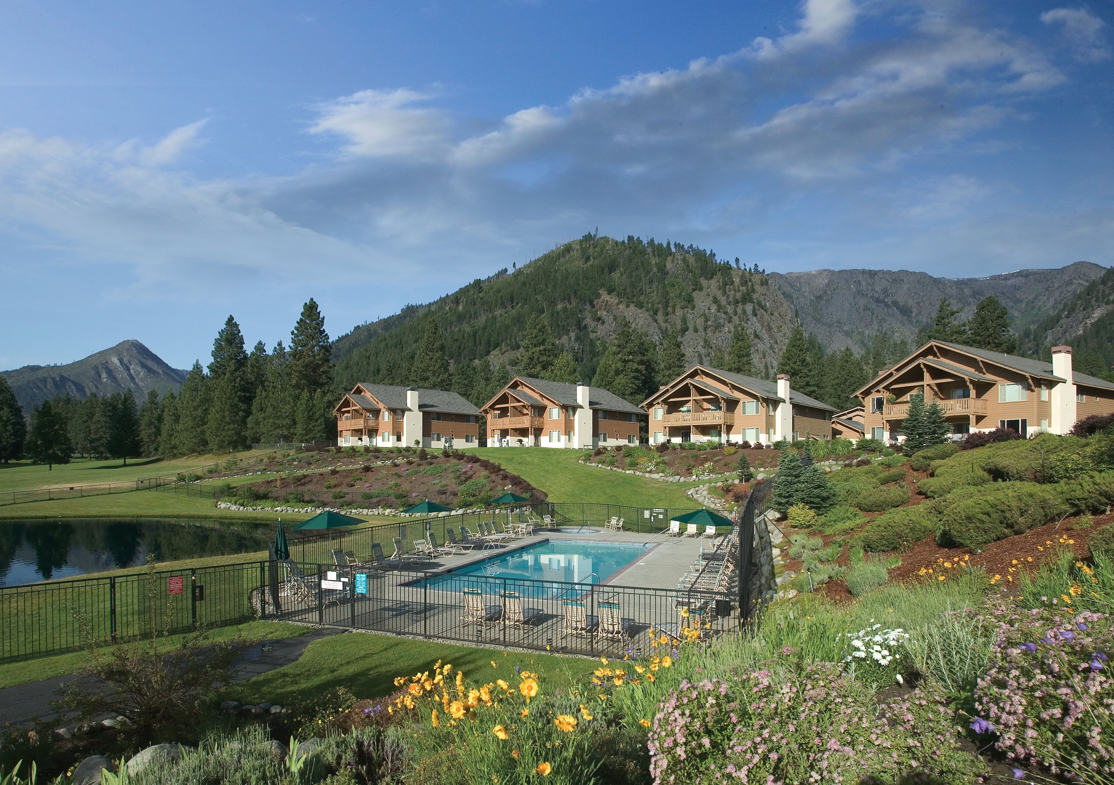 Un resort con varias edificaciones de estilo cabaña, una piscina y un lago.