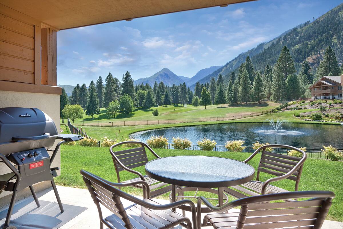 Eine Außenpatio mit Grill, Tisch und Stühlen mit Blick auf einen See und Berge.