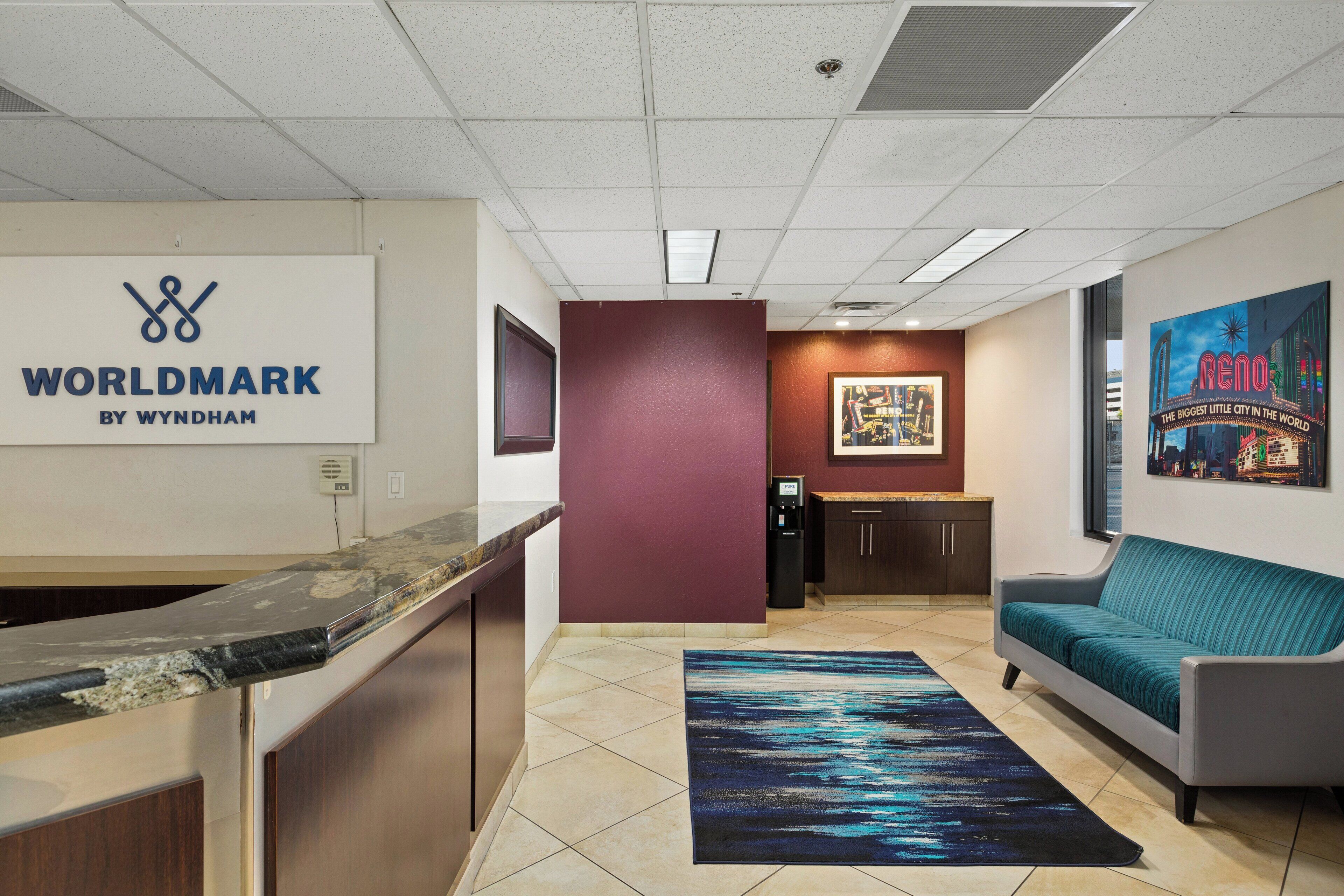 A reception area with a marble counter, a red accent wall, a framed cityscape poster, a teal sofa, and a rug with a cityscape design.