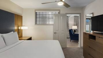 A hotel room with a bed, a nightstand, a desk, a chair, a television, and a ceiling fan.