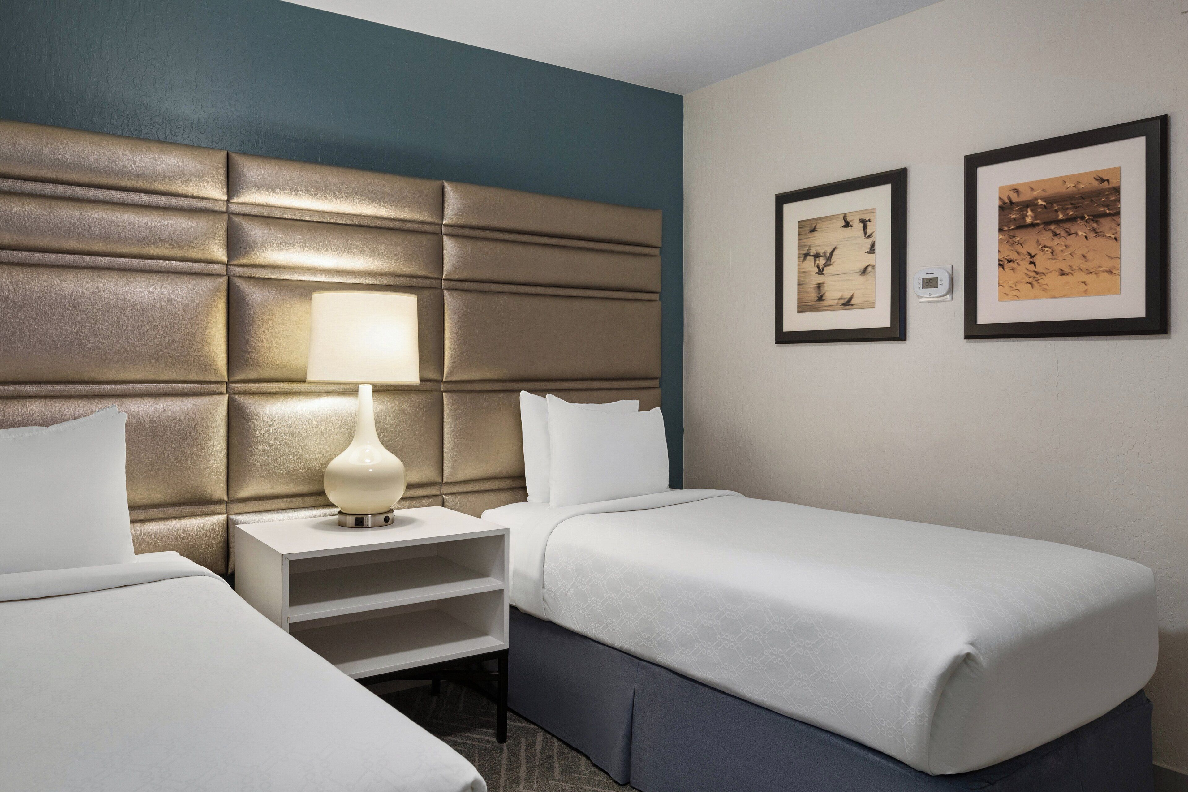 A hotel room with two beds, a nightstand with a lamp, and two framed pictures on the wall.