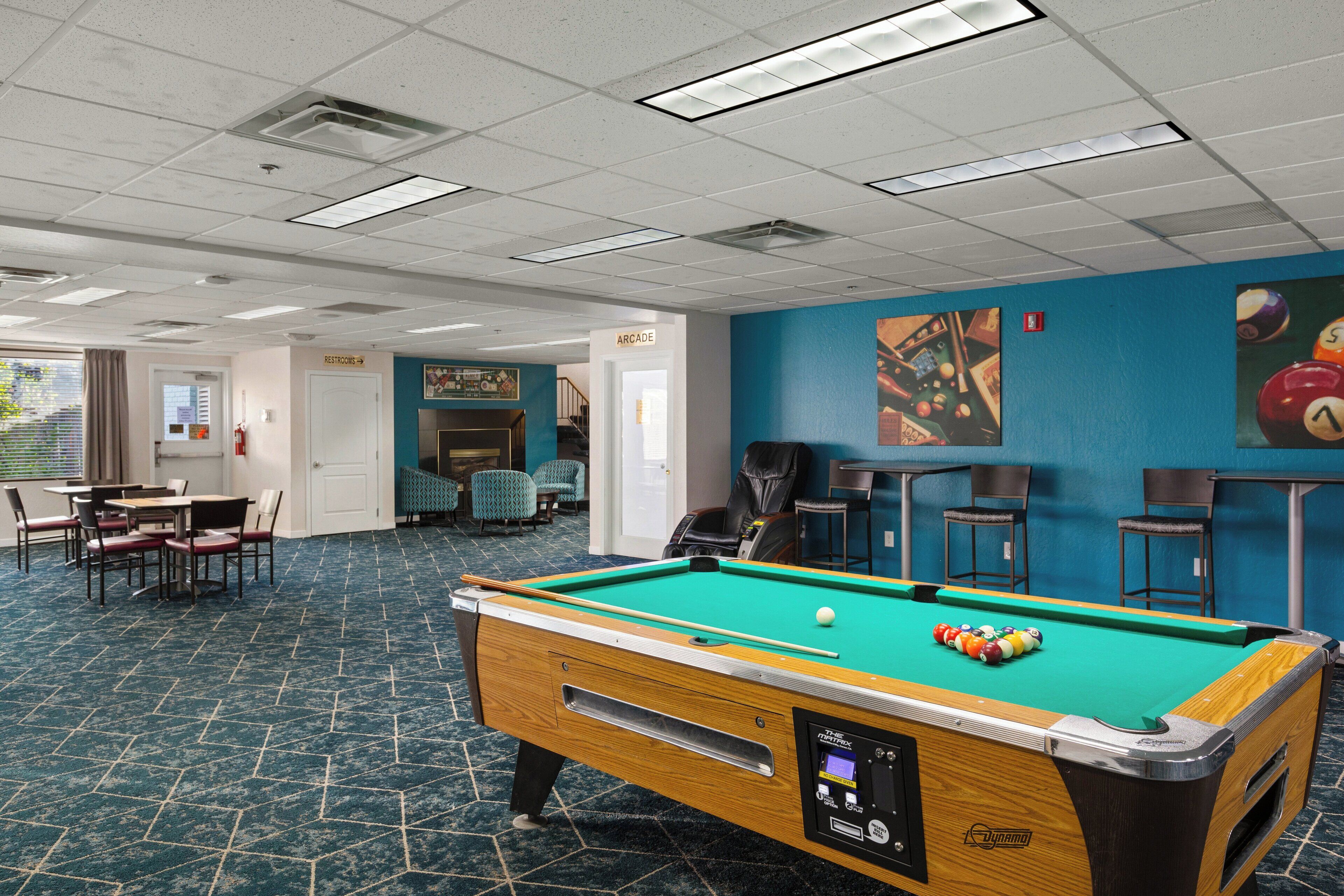 A pool table with a ball, a pool cue, and a seating area with chairs and tables.