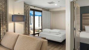Hotelkamer met een bank, een bed, een nachtkastje, een lamp en uitzicht op de stad door een groot raam.