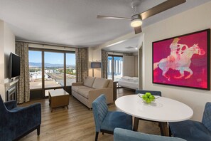 A modern hotel room with a large window, a flat-screen TV, a round dining table with blue chairs, a sofa, and a ceiling fan. - WorldMark Reno (Reno)