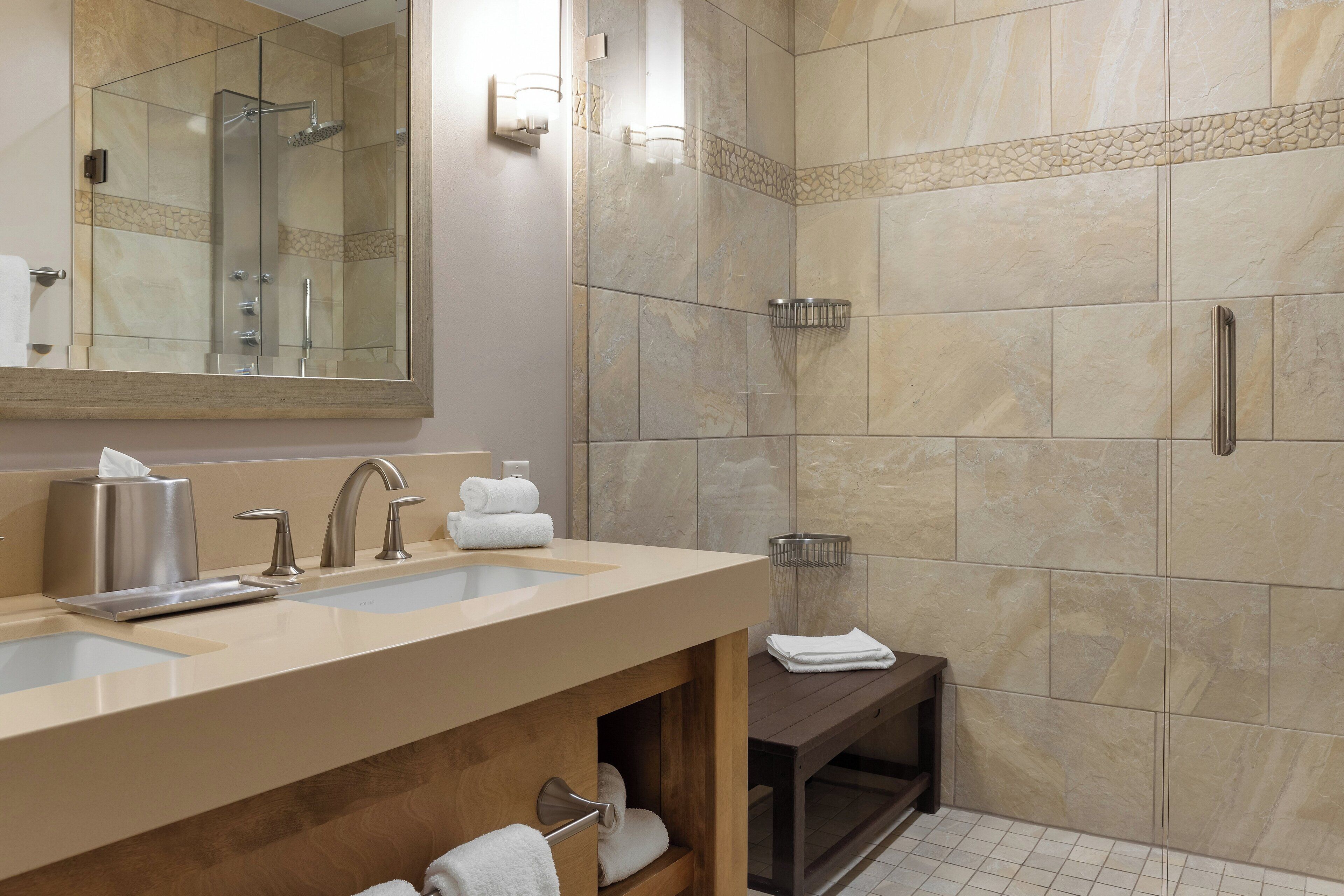 A modern bathroom with a large mirror, two sinks, a shower, and a towel rack.