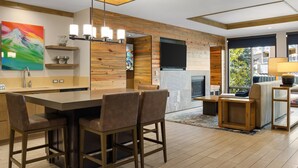 A modern kitchen with a wooden accent wall, a large island with bar stools, a flat-screen TV, and a fireplace. - Club Wyndham Resort at Avon (Avon)