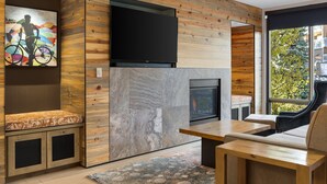 A modern living room with a fireplace, wooden paneling, a mounted TV, and a seating area with a view of the outdoors. - Club Wyndham Resort at Avon (Avon)