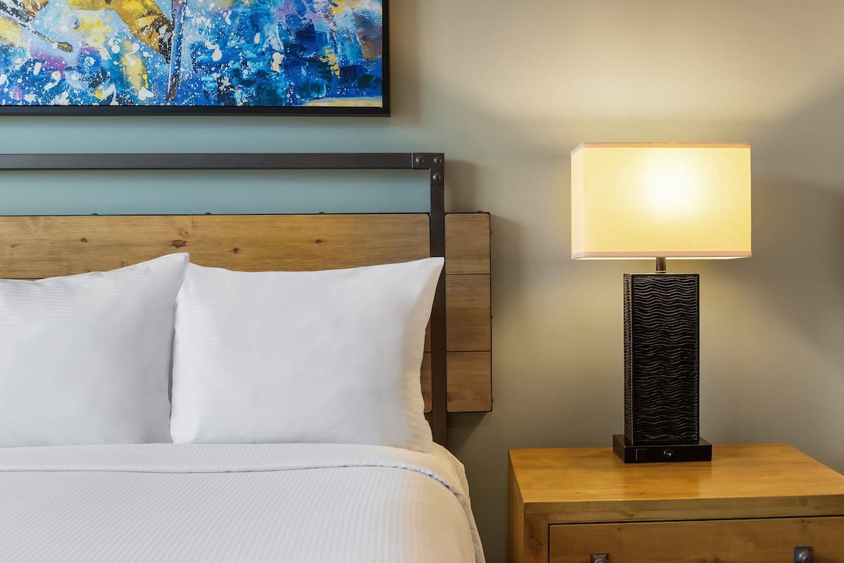 A neatly made bed with white linens, a wooden headboard, and a bedside table with a lamp.