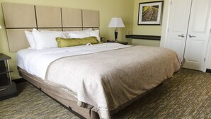 A neatly made bed with a patterned bedspread, a bedside table with a lamp, and a door in the background.
