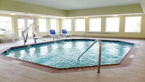 Una piscina interior con trampolín, dos sillones de descanso y una mesa con sillas.