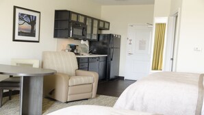 A compact hotel room with a kitchenette, a dining area, and a bed.