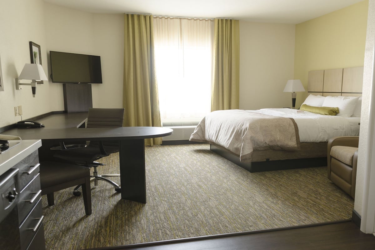 Habitación de hotel con cama, escritorio, silla, televisor y ventana con cortinas.
