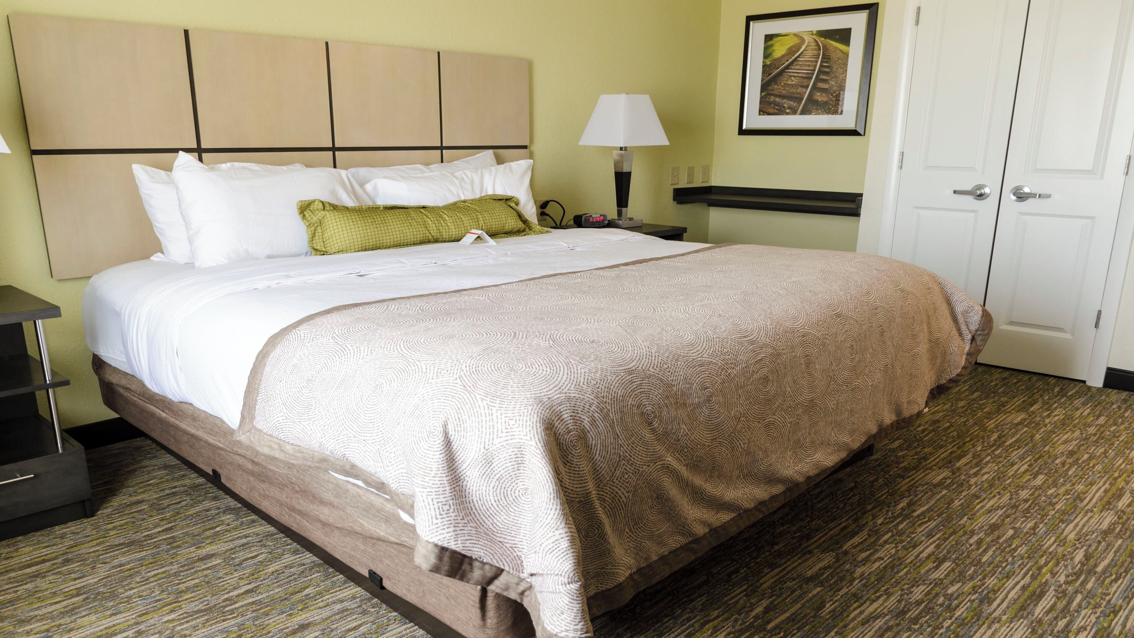 A hotel room with a bed, a nightstand, a lamp, a clock, and a door.