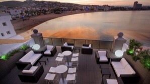 Terraza en la azotea con mobiliario exterior, con vistas a la playa y al paisaje urbano al atardecer.