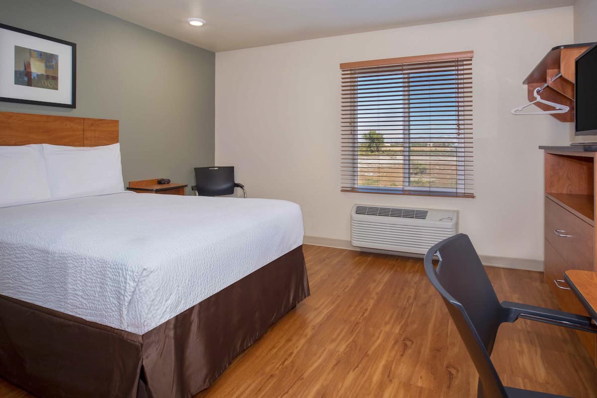 Ein Hotelzimmer mit einem großen Bett, einem Schreibtisch mit Stuhl, einem Fernseher und einem Fenster mit Jalousien.