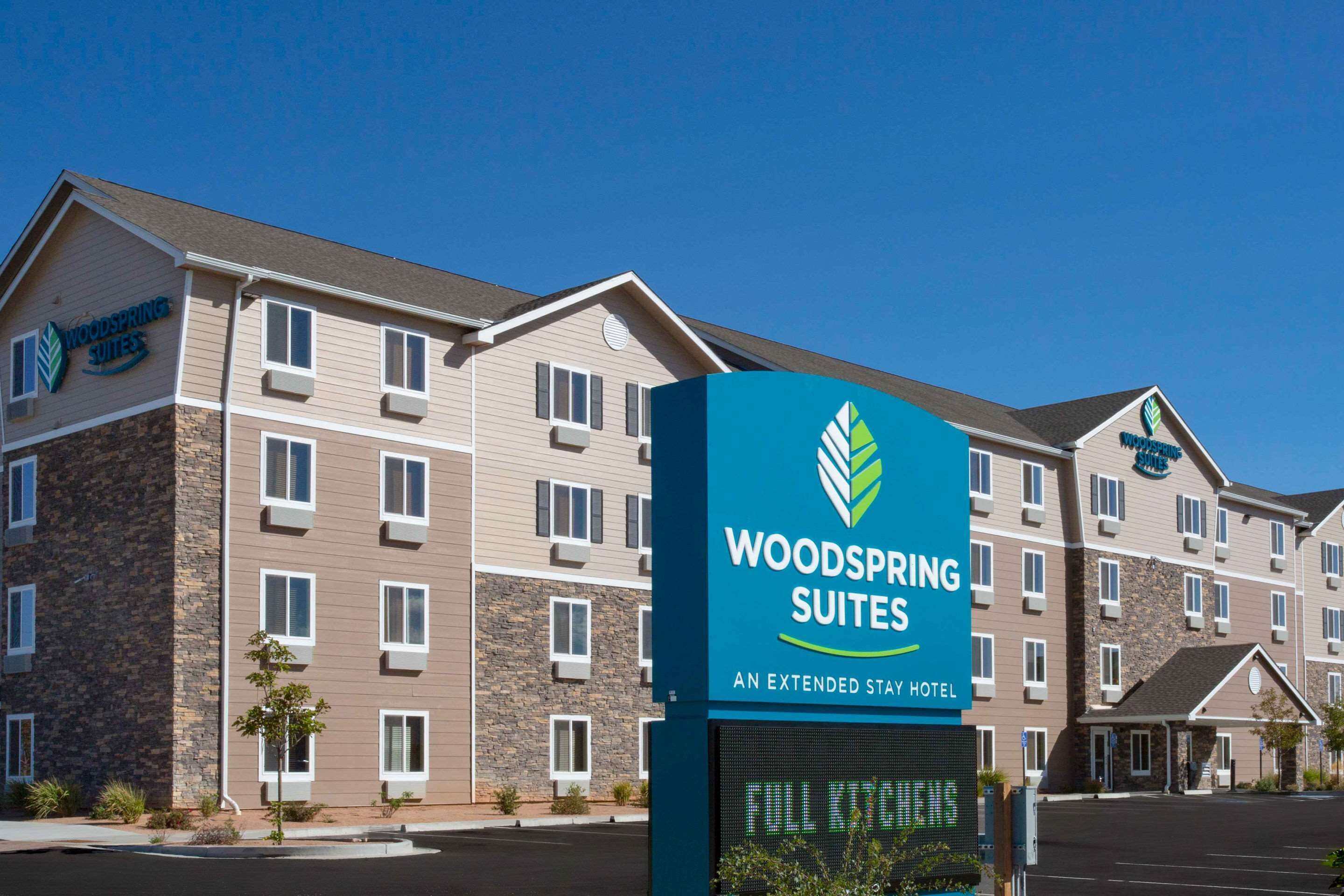 A hotel with a sign reading "Woodspring Suites" and "An Extended Stay Hotel" indicating it is a full-service hotel.