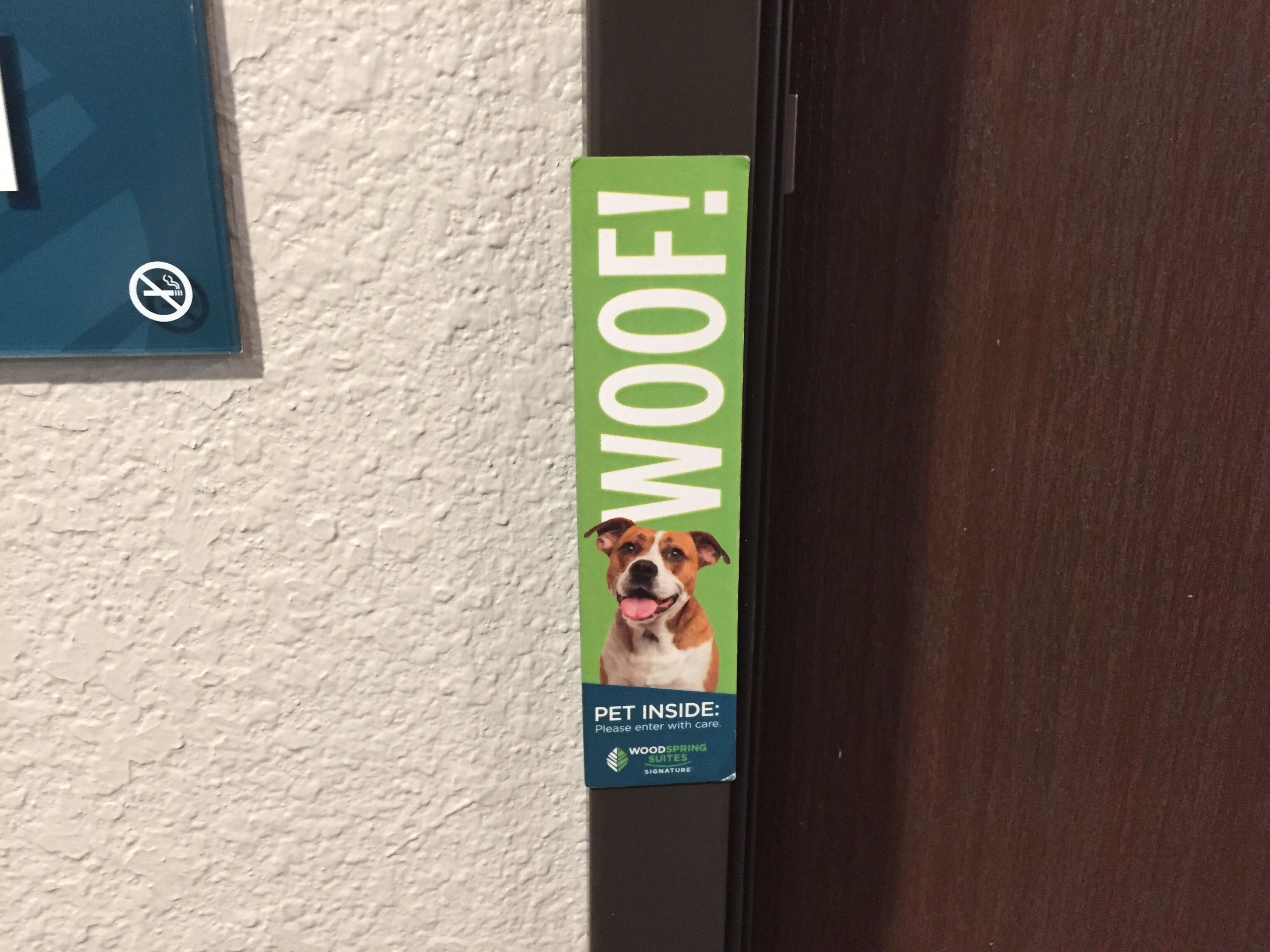 A door with a green sign featuring a dog and the text "WOOF! PET INSIDE: Please enter with care. WOODS SPRING SUITES SIGNATURE".
