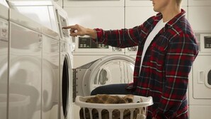 Une personne utilisant un lave-linge à chargement frontal dans une laverie en libre-service équipée de plusieurs machines.