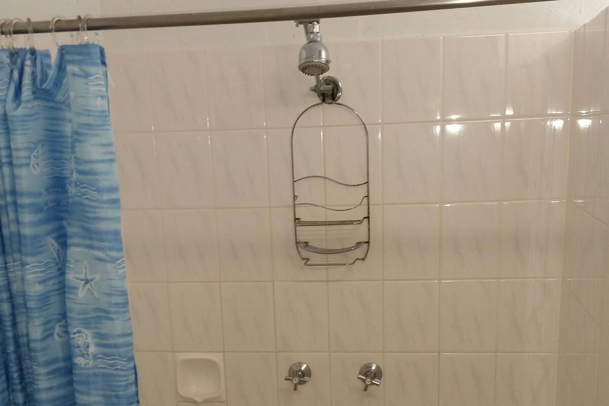 A shower area with a blue shower curtain, a showerhead, and two faucets.