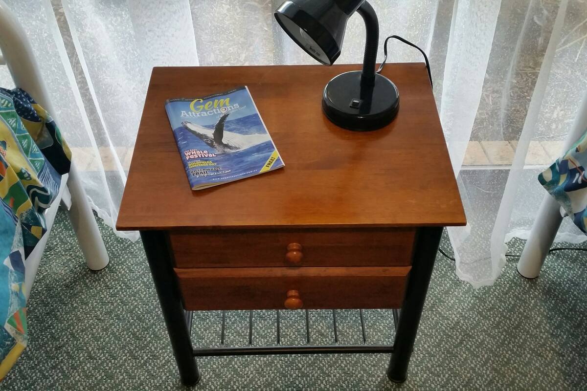A small wooden nightstand with a book titled "Gem Attractions" and a black desk lamp.