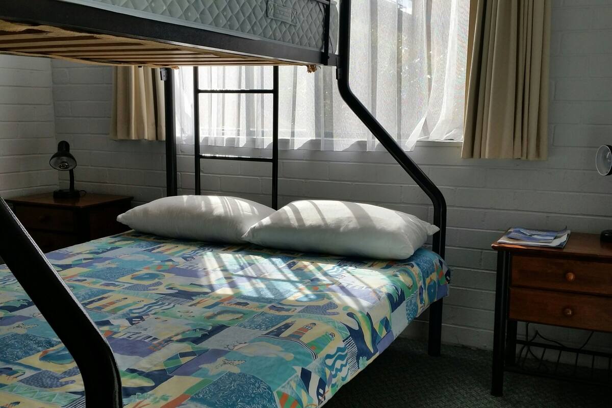 A bunk bed with a colorful bedspread, a bedside table with a lamp, and a window with curtains.