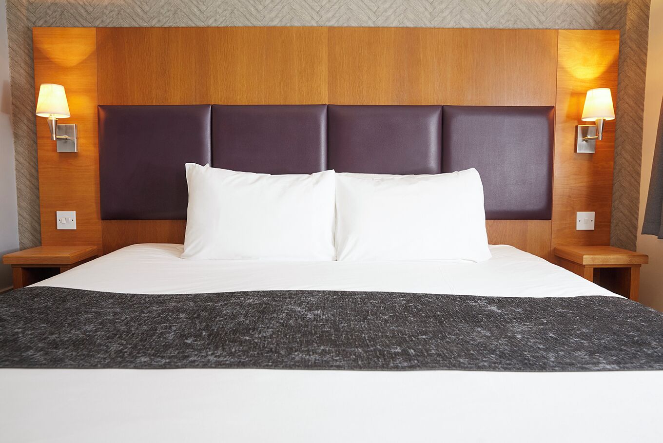 A hotel room with a large bed, two bedside tables, and wall-mounted lamps.
