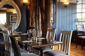 A dining table set for four with chairs, a mirror, and a wooden column in the background. - De Trafford Hotel by Chef and Brewer Collection (Alderley Edge)
