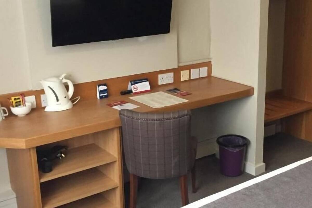 Habitación de hotel con un escritorio de madera, una silla, un televisor, una tetera, un cesto de basura y un estante pequeño.
