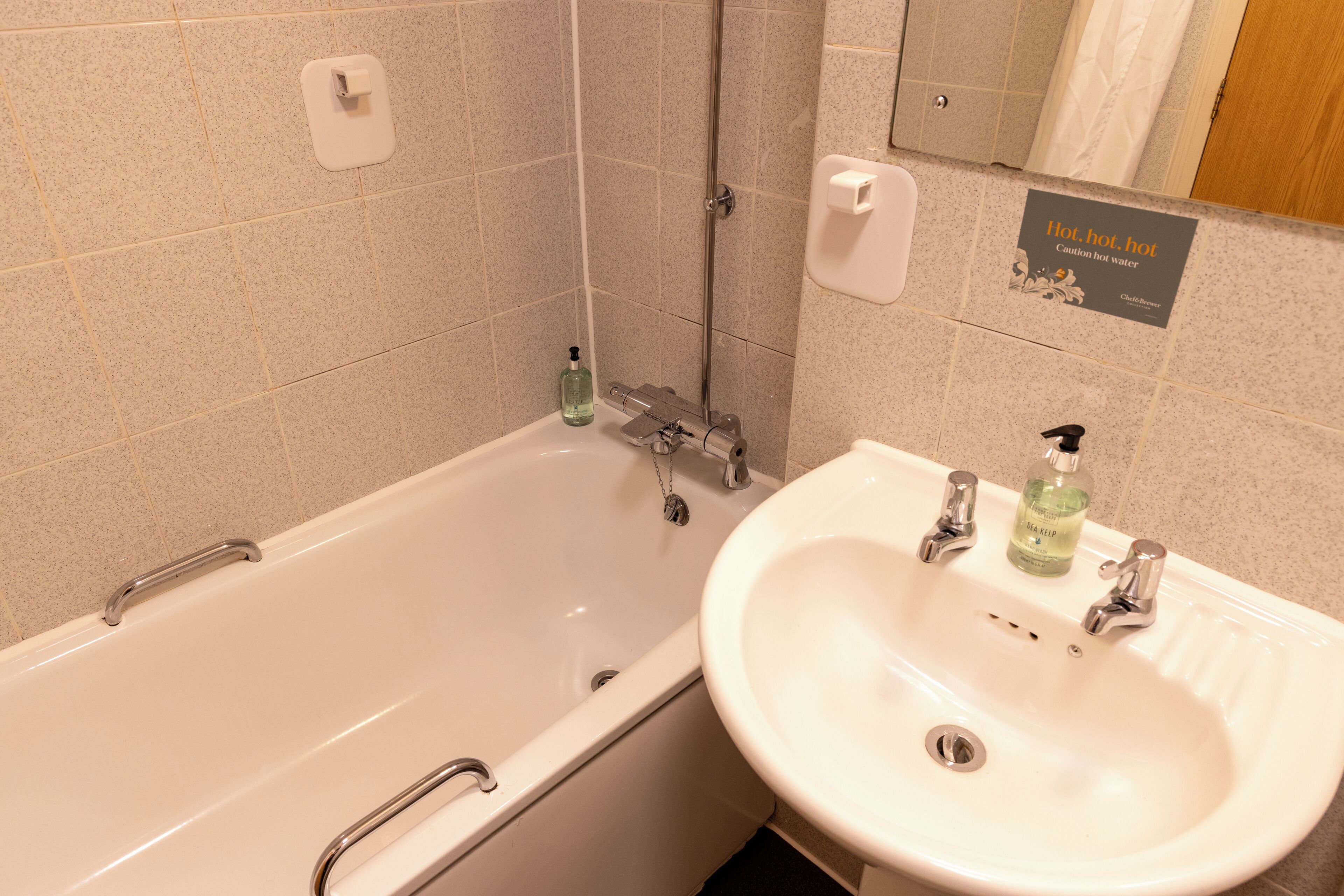 A bathroom with a bathtub, a sink, and a caution sign for hot water.
