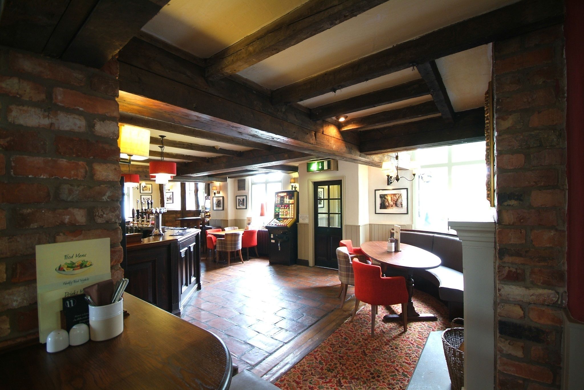 A cozy restaurant with exposed wooden beams, brick walls, and a mix of red and white furniture.
