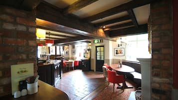 A cozy restaurant with exposed wooden beams, brick walls, and a mix of red and white furniture.