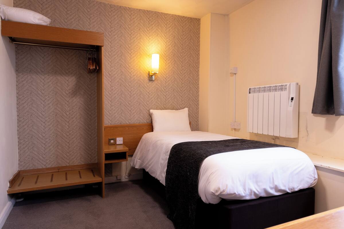 Habitación de hotel con literas, una mesita de noche, una lámpara de pared y un radiador.