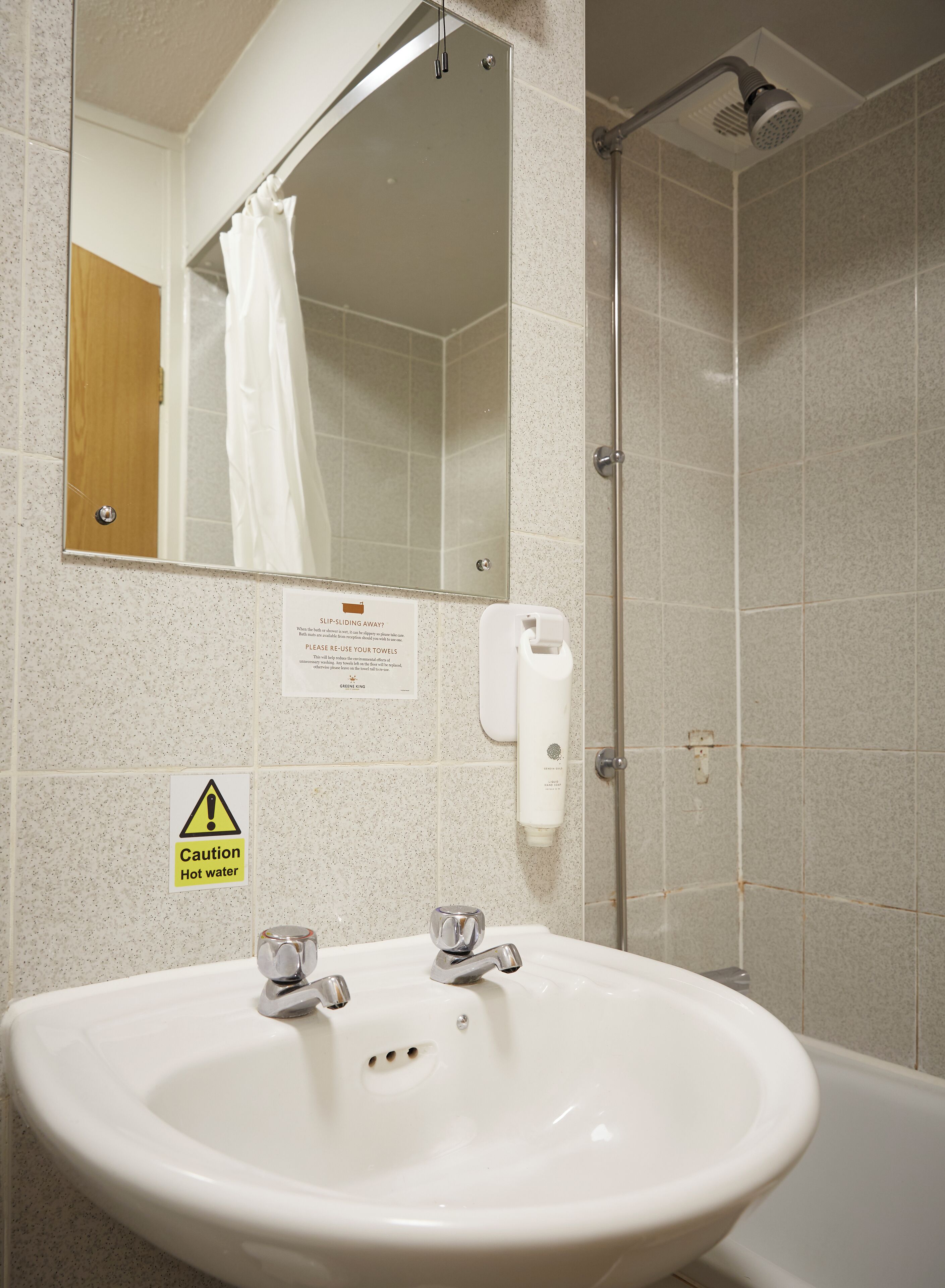 Een badkamer met een wastafel, spiegel, douche en waarschuwingsborden.
