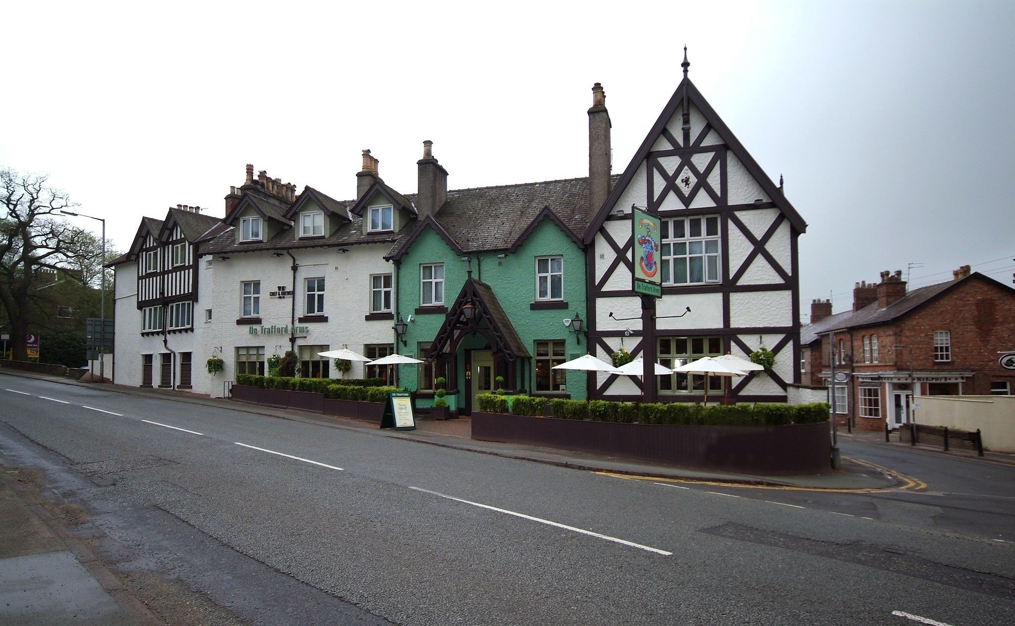 A traditional Tudor-style building with a green and white facade, multiple chimneys, and a prominent entrance with umbrellas.